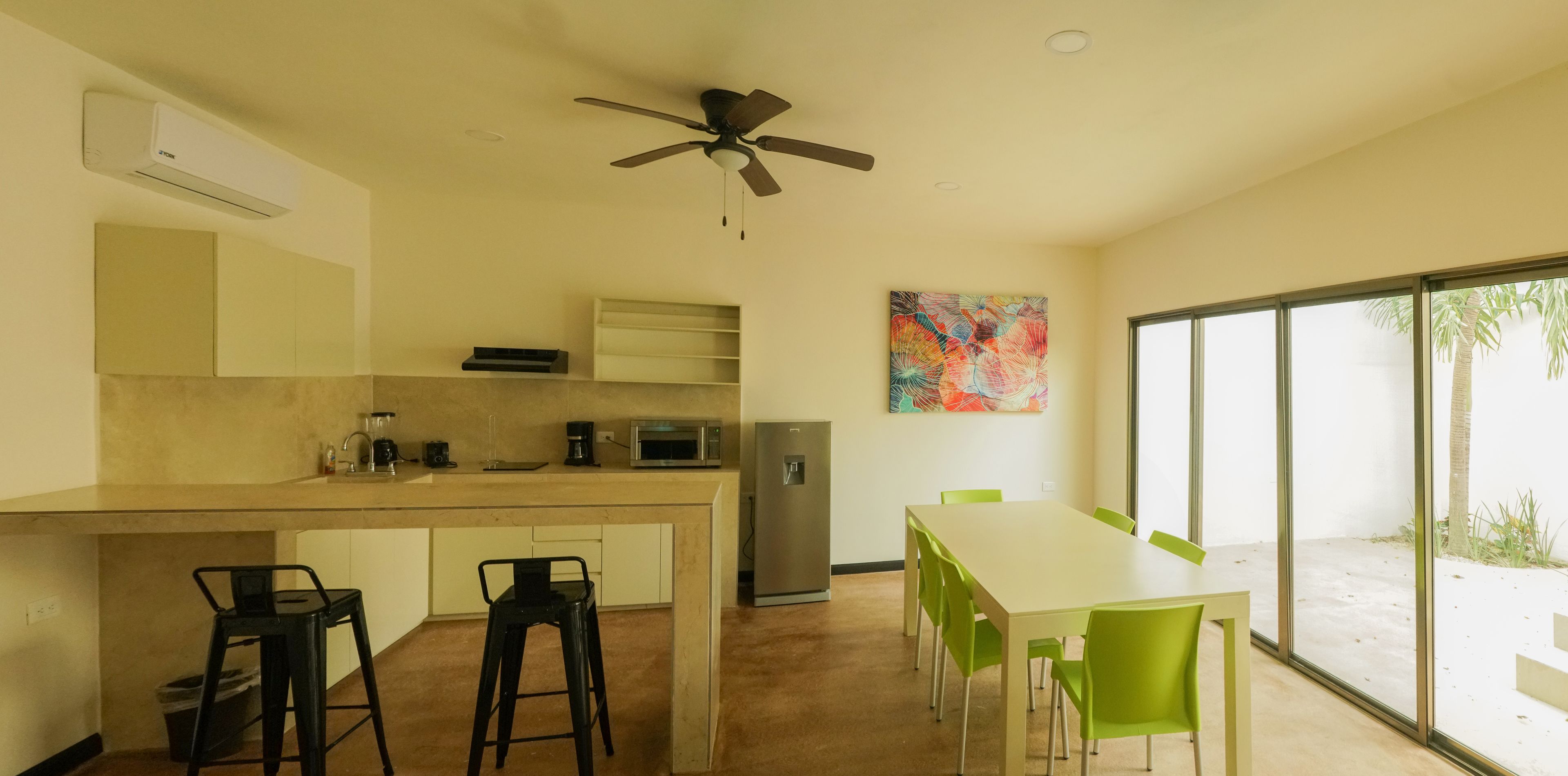 Una cucina moderna con zona pranzo, ventilatore a soffitto e un'ampia finestra vista palme.