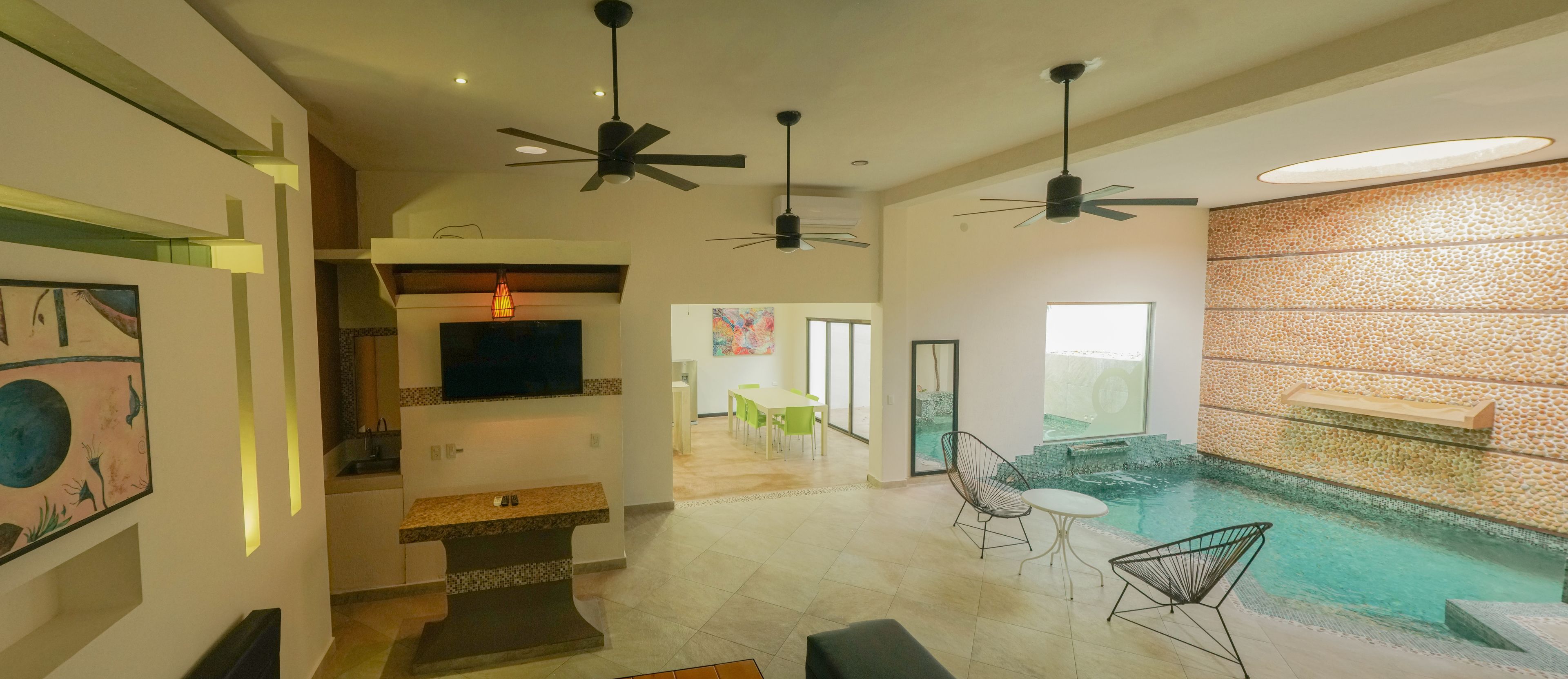 Un amplio salón con piscina, ventiladores de techo y una cocina moderna.