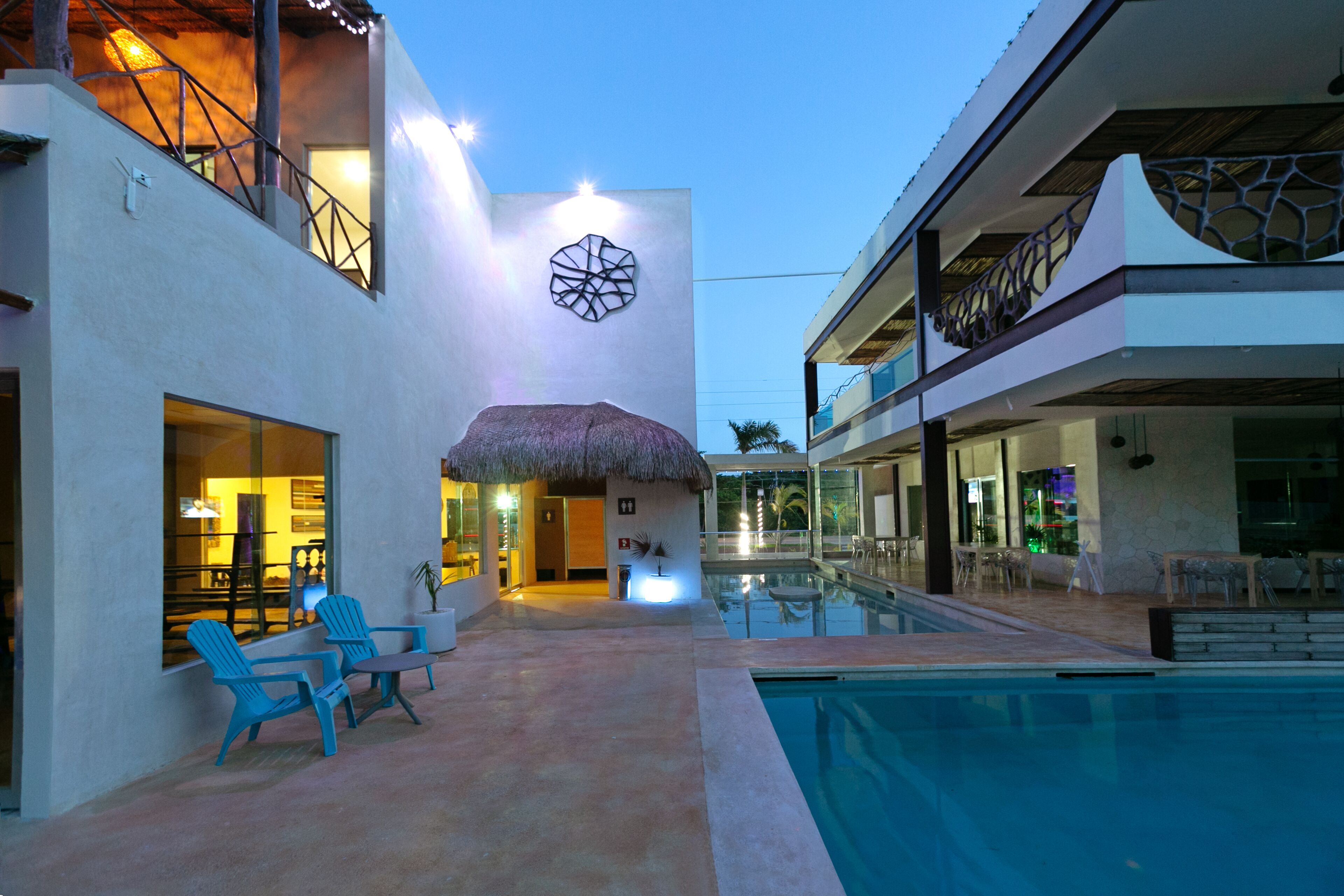 A modern building with a pool, outdoor seating, and a thatched-roof entrance.