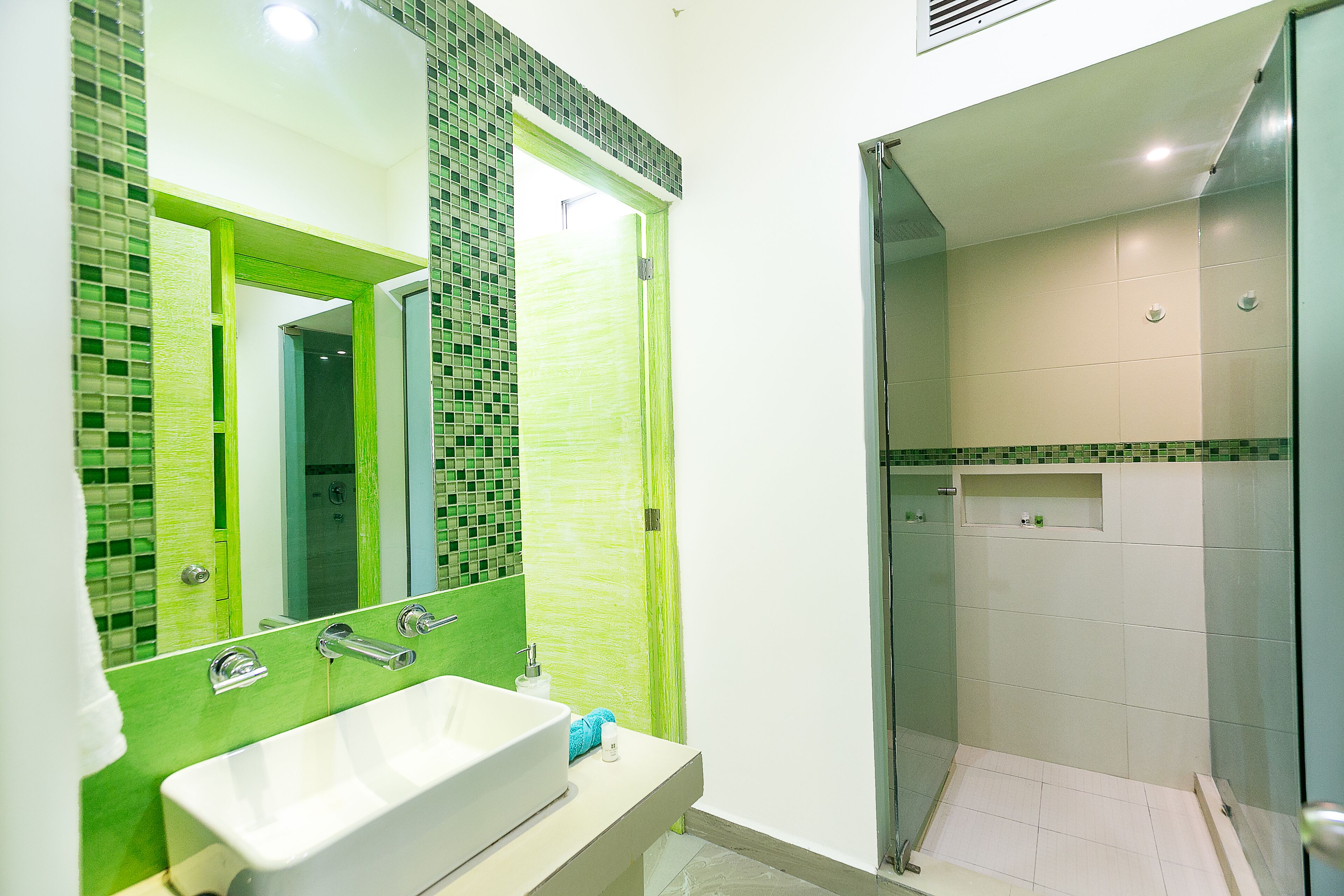 A bathroom with a white sink, green-tiled walls, and a glass shower enclosure.