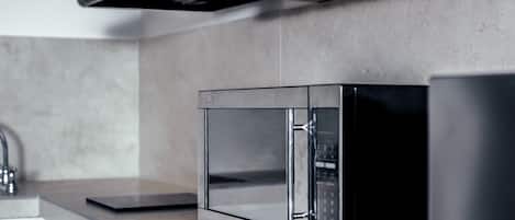 A modern kitchen with a stainless steel microwave, a black range hood, and a marble countertop.