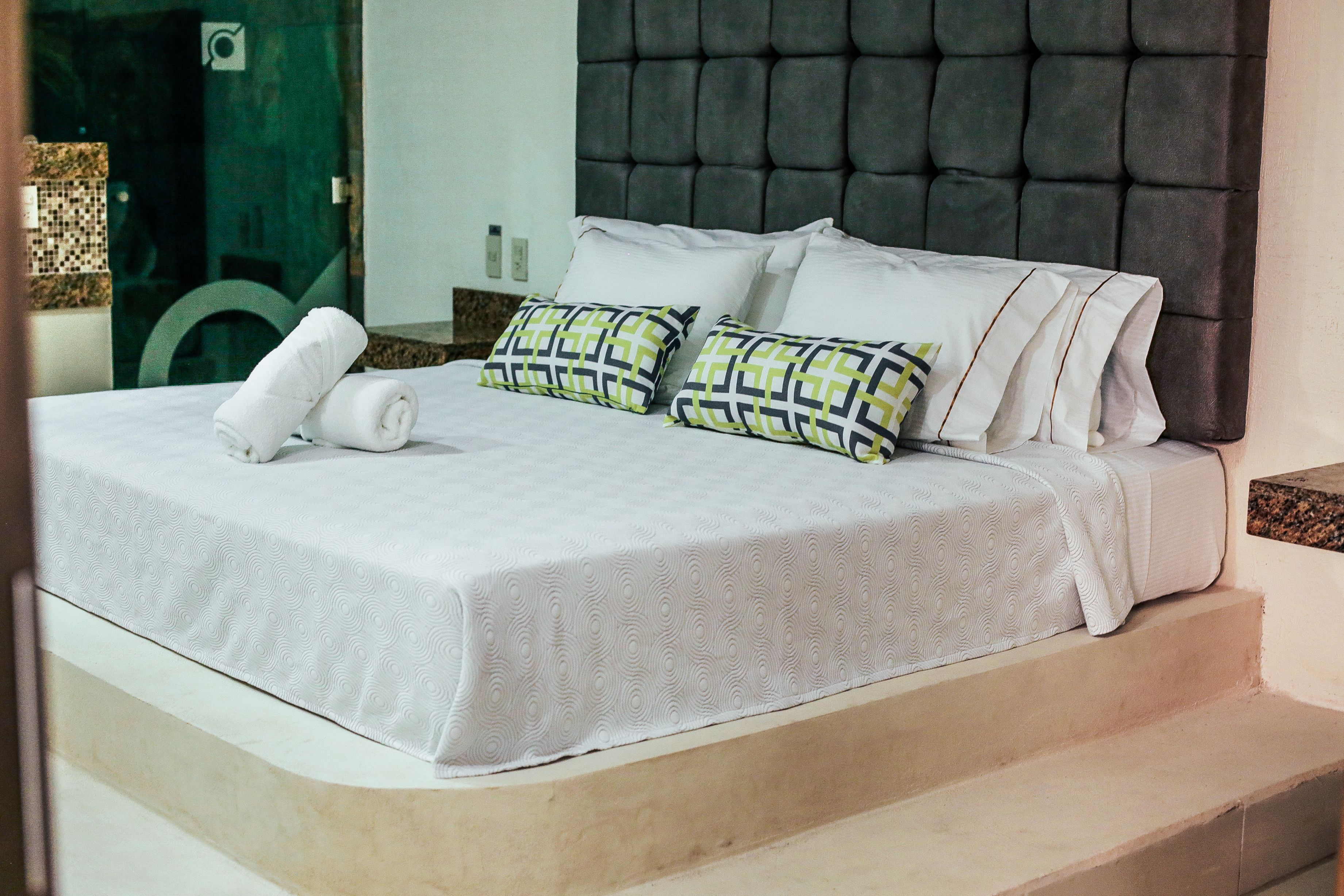 A neatly made bed with a white bedspread and two patterned pillows, a dark upholstered headboard, and a small towel on the bed.
