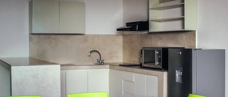Una cocina moderna con armarios blancos, un lavamanos, un microondas y un refrigerador. Hay dos sillas verdes alrededor de una mesa.