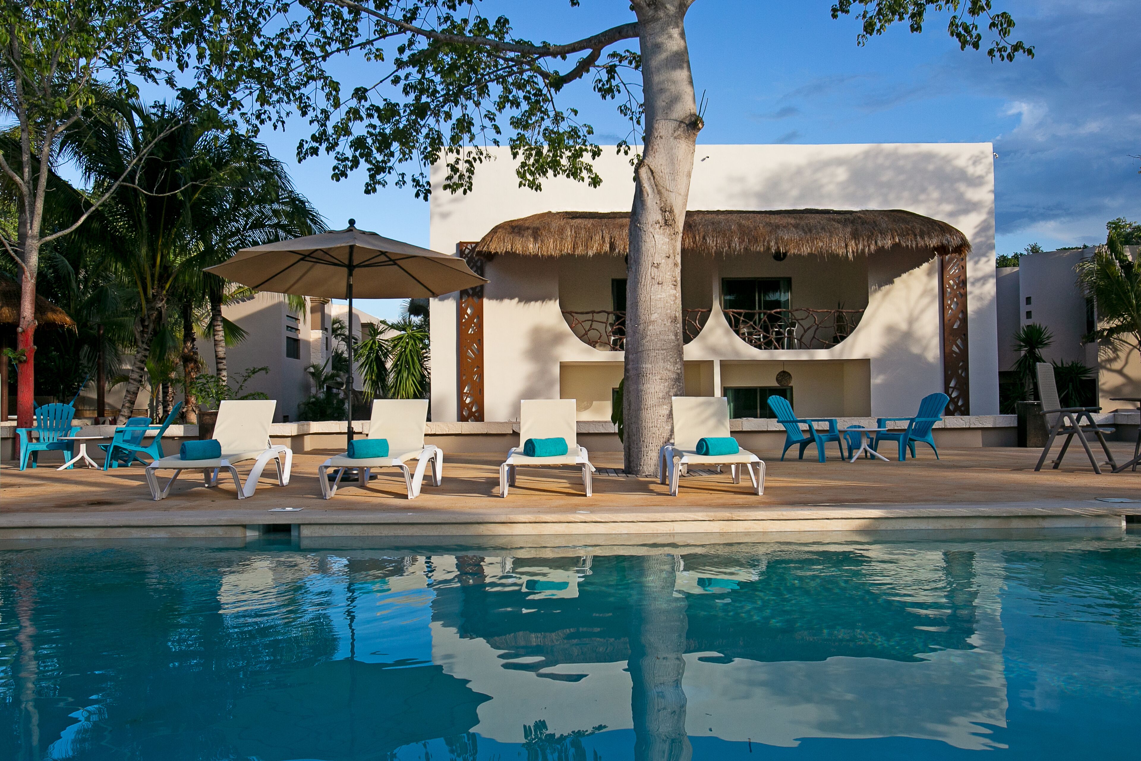 A poolside area with lounge chairs, a thatched-roof structure, and a clear pool.