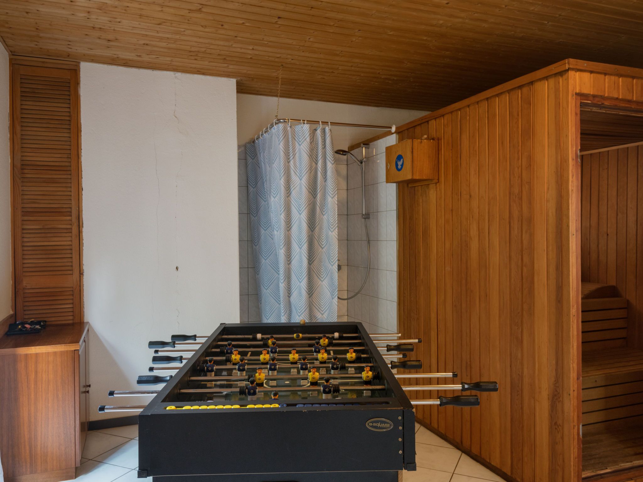 A room with a foosball table, a wooden cabinet, and a shower area.
