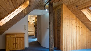 Un dormitorio con techo inclinado, paredes de madera, una cama, un armario y un pasillo que conduce a otra habitación.