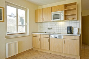A kitchen with wooden cabinets, a microwave, a sink, and a window. - House Martha - Fritz - House Martha (Ahrenshoop)