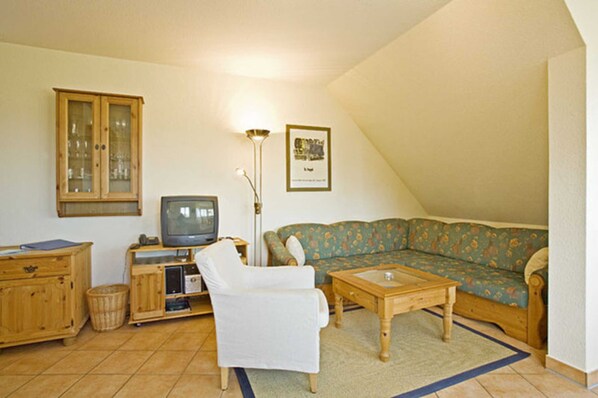 A living room with a television, sofa, armchair, and wooden cabinet.