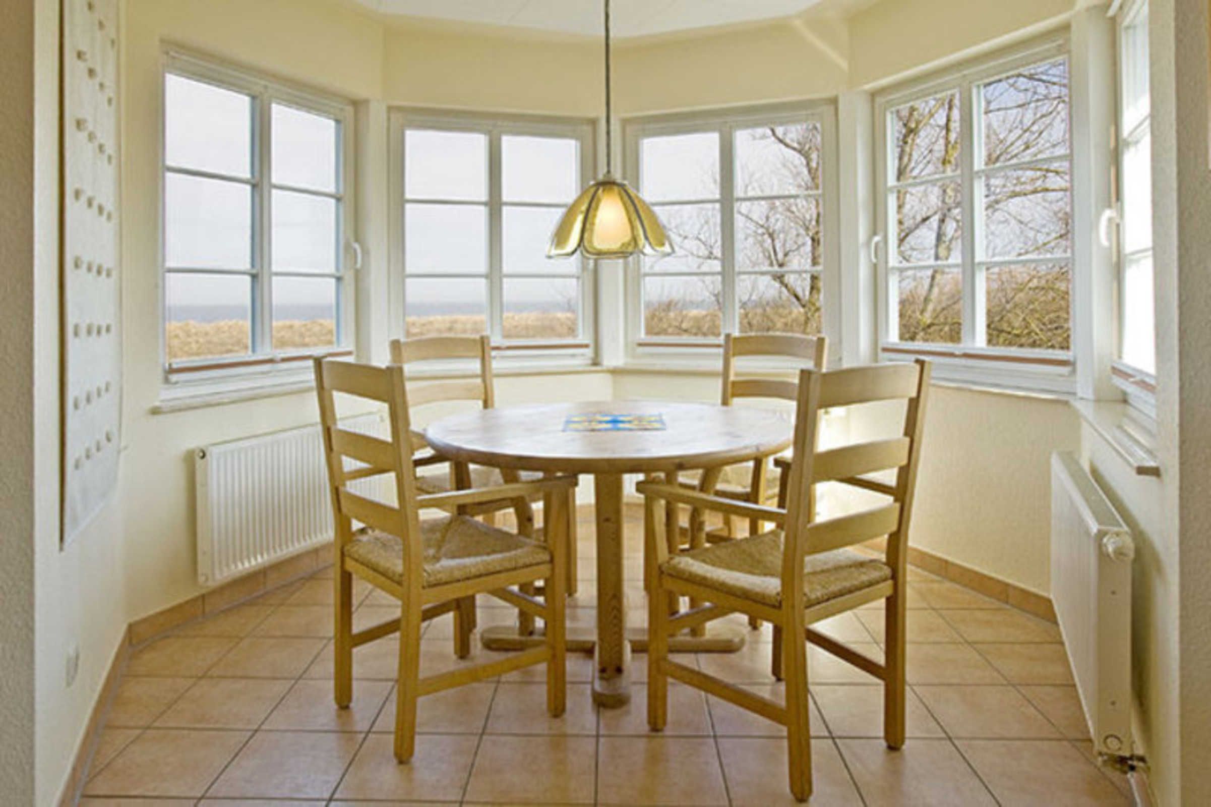Comedor con mesa redonda y seis sillas, ventanas amplias y lámpara colgante.