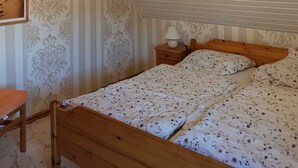 Ein Schlafzimmer mit schrägem Dach, einem Bett mit floralem Bettzeug, einem Nachttisch mit Lampe und einem Bild an der Wand.