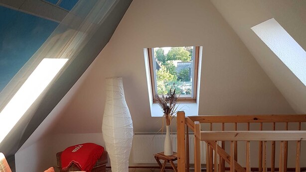 Ein gemütliches Dachzimmer mit schrägen Wänden, einem Karosobasofa, einem kleinen Tisch mit einer Tischdecke im blau-maritimen Stil und einem Holckrippenbett.