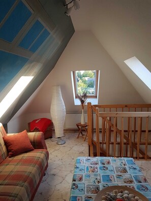 A cozy attic room with a sloped ceiling, a plaid sofa, a small table with a blue ocean-themed tablecloth, and a wooden crib.