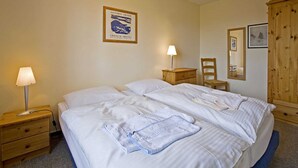 Camera d'albergo con un letto matrimoniale, un comodino in legno con una lampada, una sedia in legno, un armadio in legno e un quadro appeso al muro.