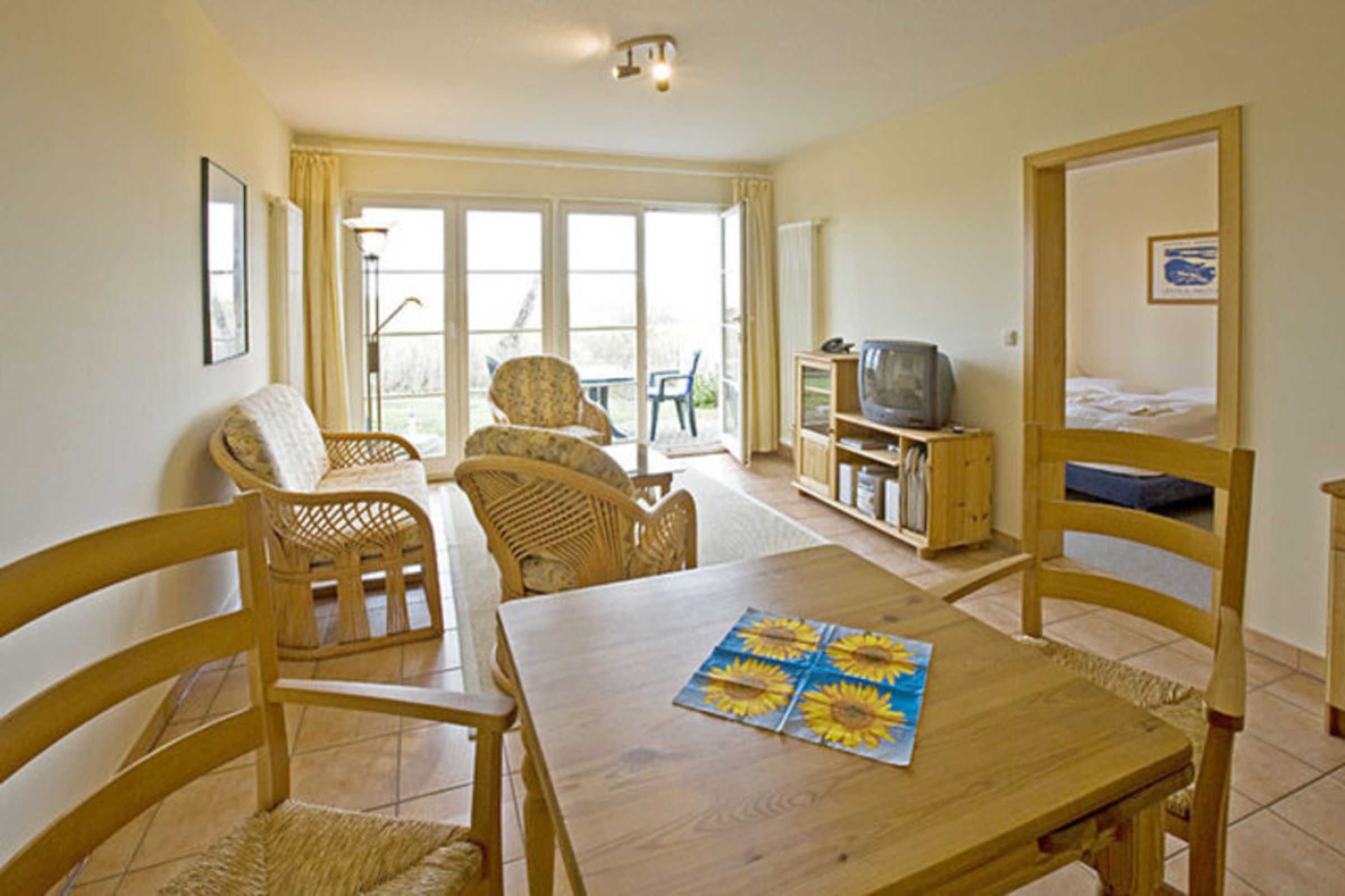 A room with a wooden table, wicker chairs, a television, and a bunk bed.