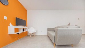Un salon moderne avec un canapé gris, un fauteuil blanc et un téléviseur à écran plat posé sur une étagère blanche.