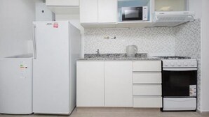Une cuisine de taille réduite avec des meubles blancs, un four à micro-ondes, une cuisinière et un réfrigérateur.