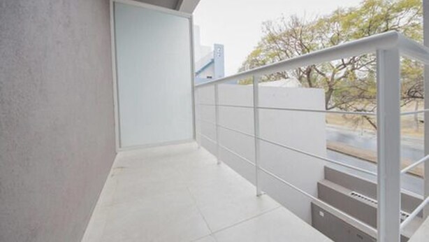 Un balcon moderne et épuré, doté d’une rambarde en métal, qui offre une vue sur les arbres et les bâtiments en arrière-plan.