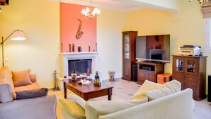A living room with a fireplace, sofa, television, and a decorative saxophone. - Villa Thea (Corfu)