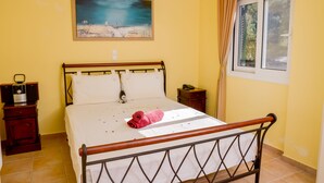 A neatly made bed with a rolled towel, a bedside table with a lamp, and a painting on the wall. - Villa Thea (Corfu)
