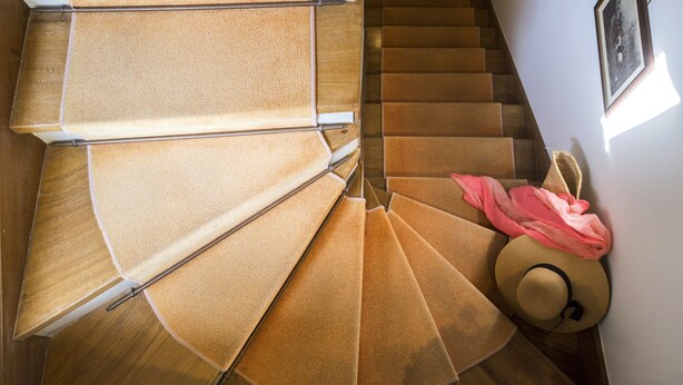 Un escalier en colimaçon avec une finition en bois et un tissu rose drapé sur la rampe.