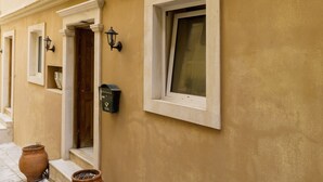 Une façade d’immeuble avec une porte, des fenêtres et deux plantes en pot, le tout sur un sol carrelé.