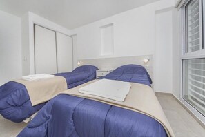 A modern hotel room with two beds, a large window, and a minimalist design.