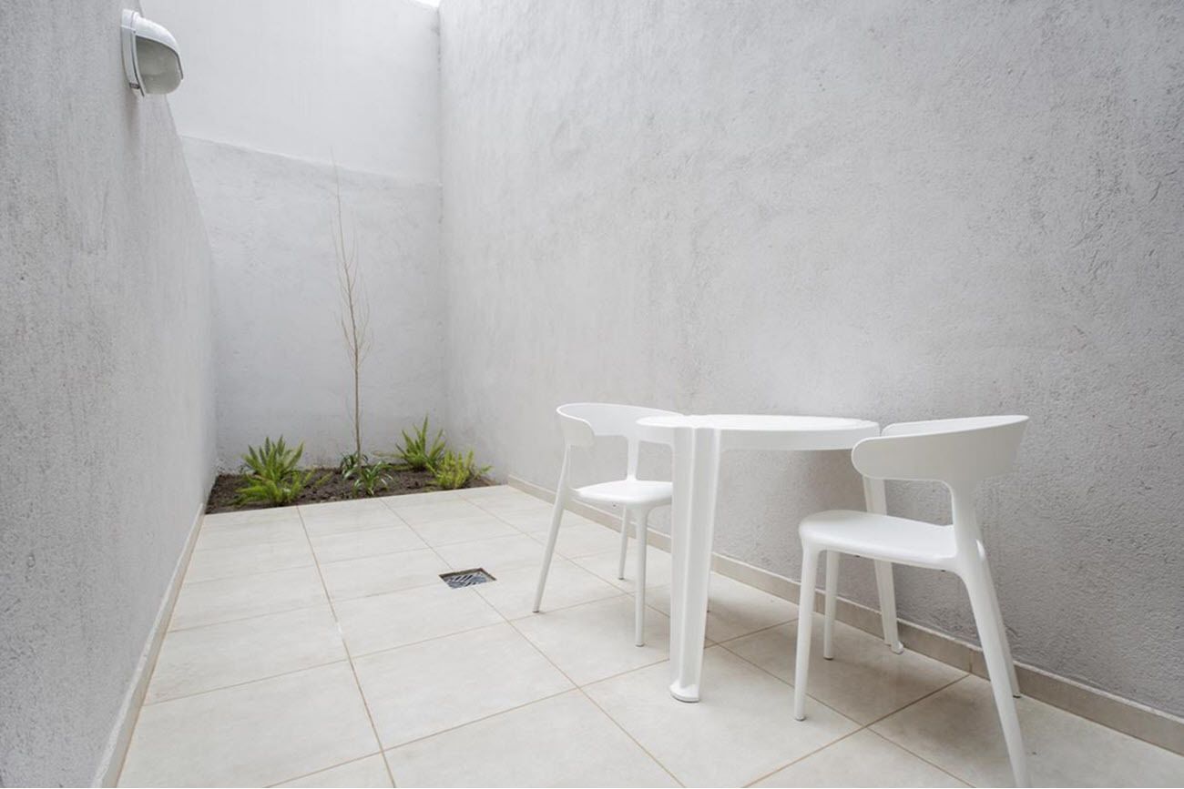 Een klein, afgesloten terras met een vloer van witte tegels, twee witte plastic stoelen en een kleine tafel.