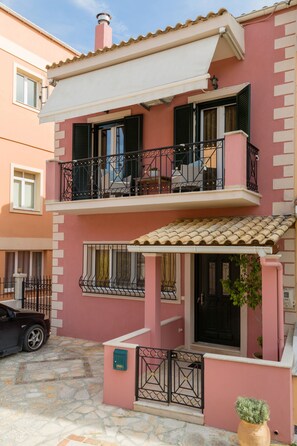 A two-story building with balconies, a tiled roof, and a stone-paved courtyard.