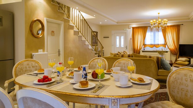 A dining area with a round table set for breakfast, a staircase, and a living room with a sofa and TV. - Suite Maison (Corfu)
