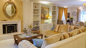 A well-lit living room with a fireplace, a sofa set, a coffee table, and a bookshelf. - Suite Maison (Corfu)