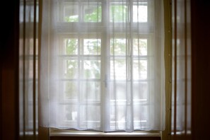 A window with a sheer white curtain partially drawn. - Srecko Apartment (Belgrade)