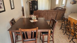 A dining area with a wooden table and chairs, a small potted plant, and a bookshelf in the background.