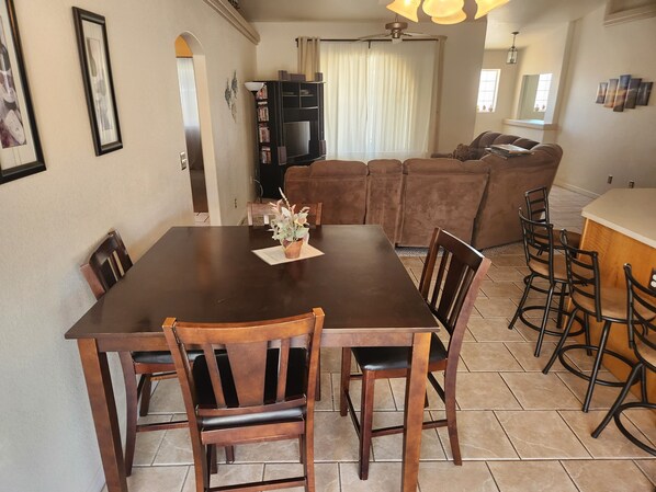 A dining area with a wooden table and chairs, a small potted plant, and a bookshelf in the background.