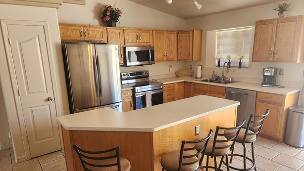 A modern kitchen with wooden cabinets, stainless steel appliances, a large island with bar stools, and a window with blinds.