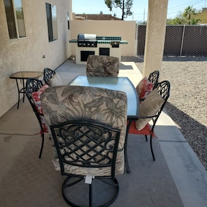 An outdoor patio with a grill, a table, and chairs.