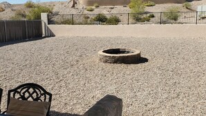An outdoor patio area with a gravel ground, a fire pit, and a view of a building with a tiled roof.