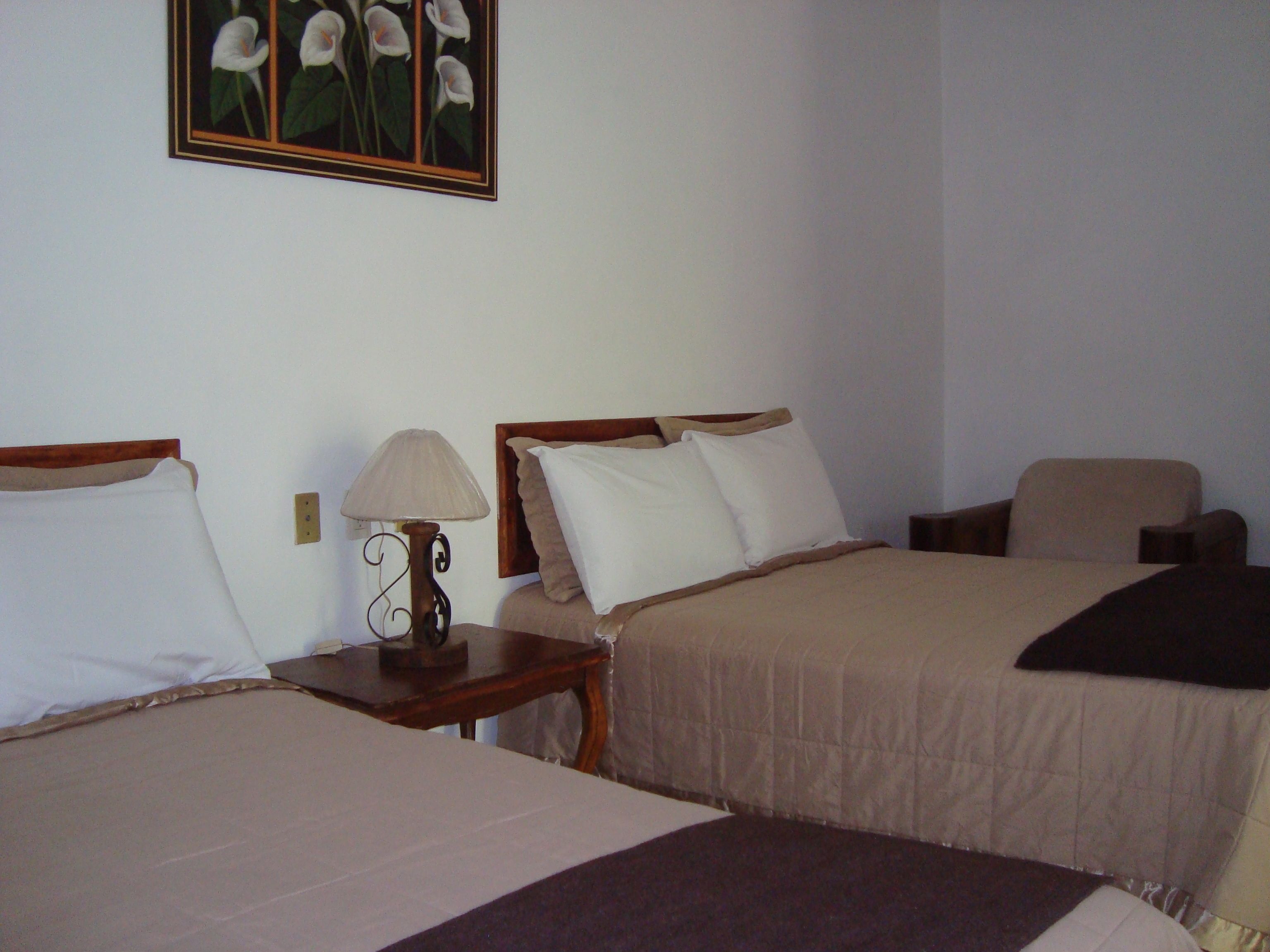 Ein Hotelzimmer mit zwei Betten, einem Nachttisch mit Lampe, einem Sessel und einem Bild an der Wand.