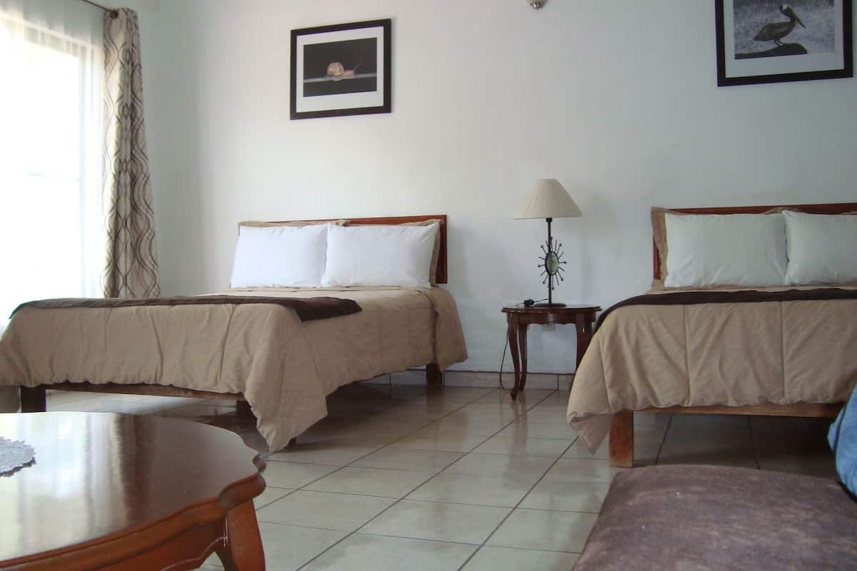 A hotel room with two beds, a small table, a lamp, and a chair.