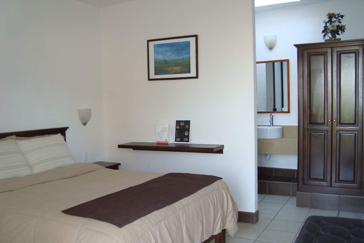 A bedroom with a bed, a nightstand, a shelf with a framed picture, a bedside table, a mirror, and a cabinet.