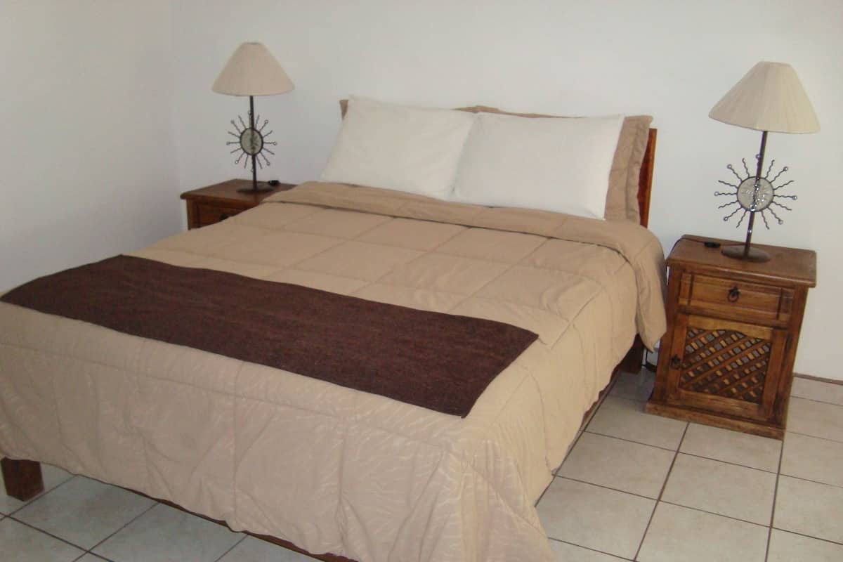 A bed with a beige bedspread and a brown throw blanket, flanked by two nightstands with lamps.
