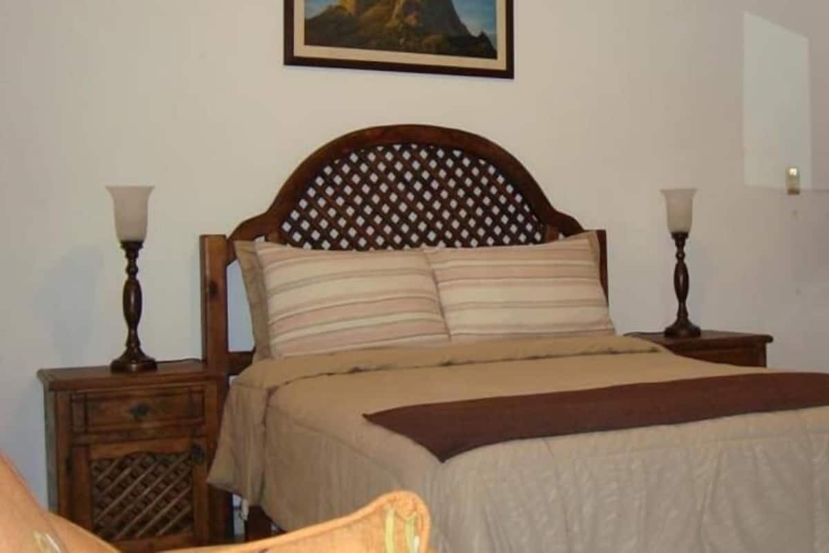 A bedroom with a wooden headboard, two bedside tables with lamps, a bed with striped bedding, a bedside table with a decorative item, a painting on the wall, and a mirror above the bed.