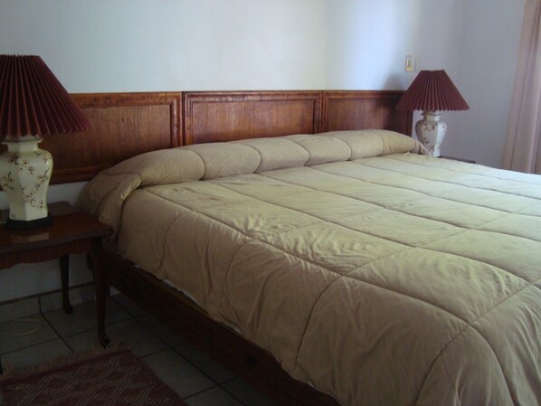 Un letto rifatto con cura, con una testiera in legno, due comodini con lampade e un tappeto sul pavimento.