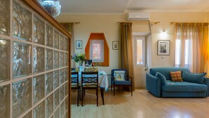 A living room with a blue sofa, a dining table with chairs, and a glass partition wall. - Heart of the old town (Corfu)