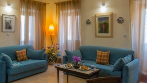 A living room with two blue sofas, a coffee table with pastries, a lamp, and a vase with flowers. - Heart of the old town (Corfu)