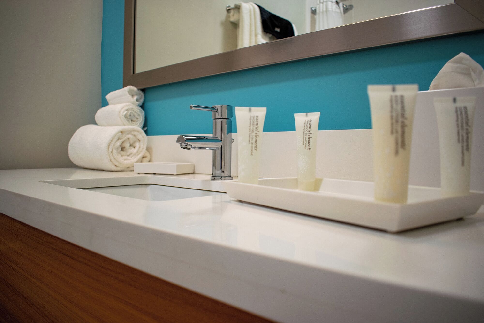 Une salle de bain avec un lavabo blanc, un miroir et des articles de toilette, notamment une serviette, un distributeur de savon et un flacon de shampoing.