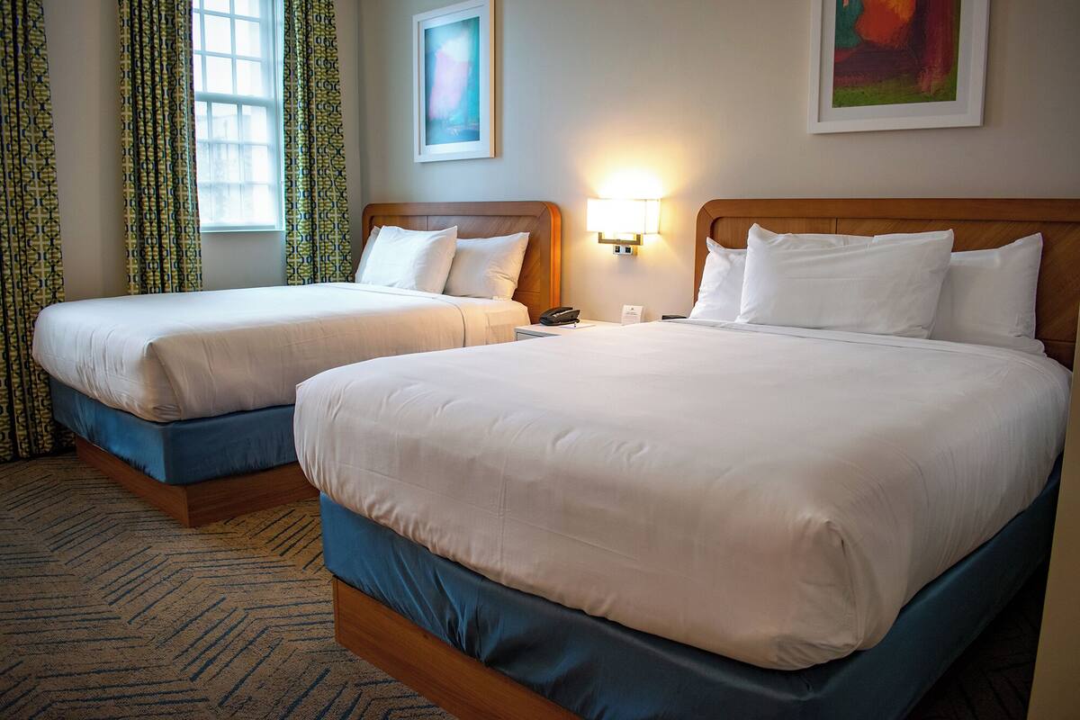 A hotel room with two beds, a nightstand with a lamp, and a painting on the wall.