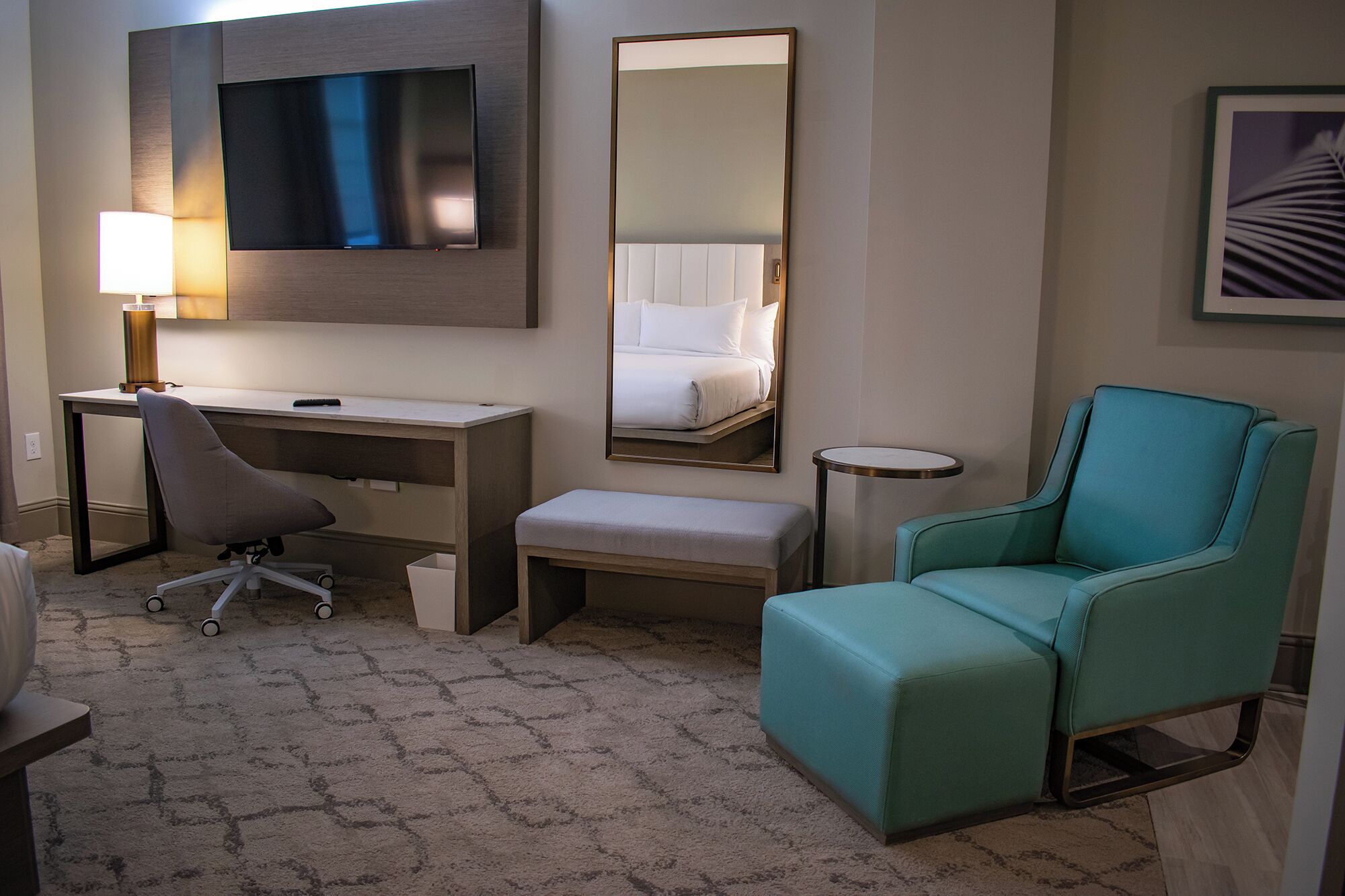 A hotel room with a desk, chair, and a large mirror.