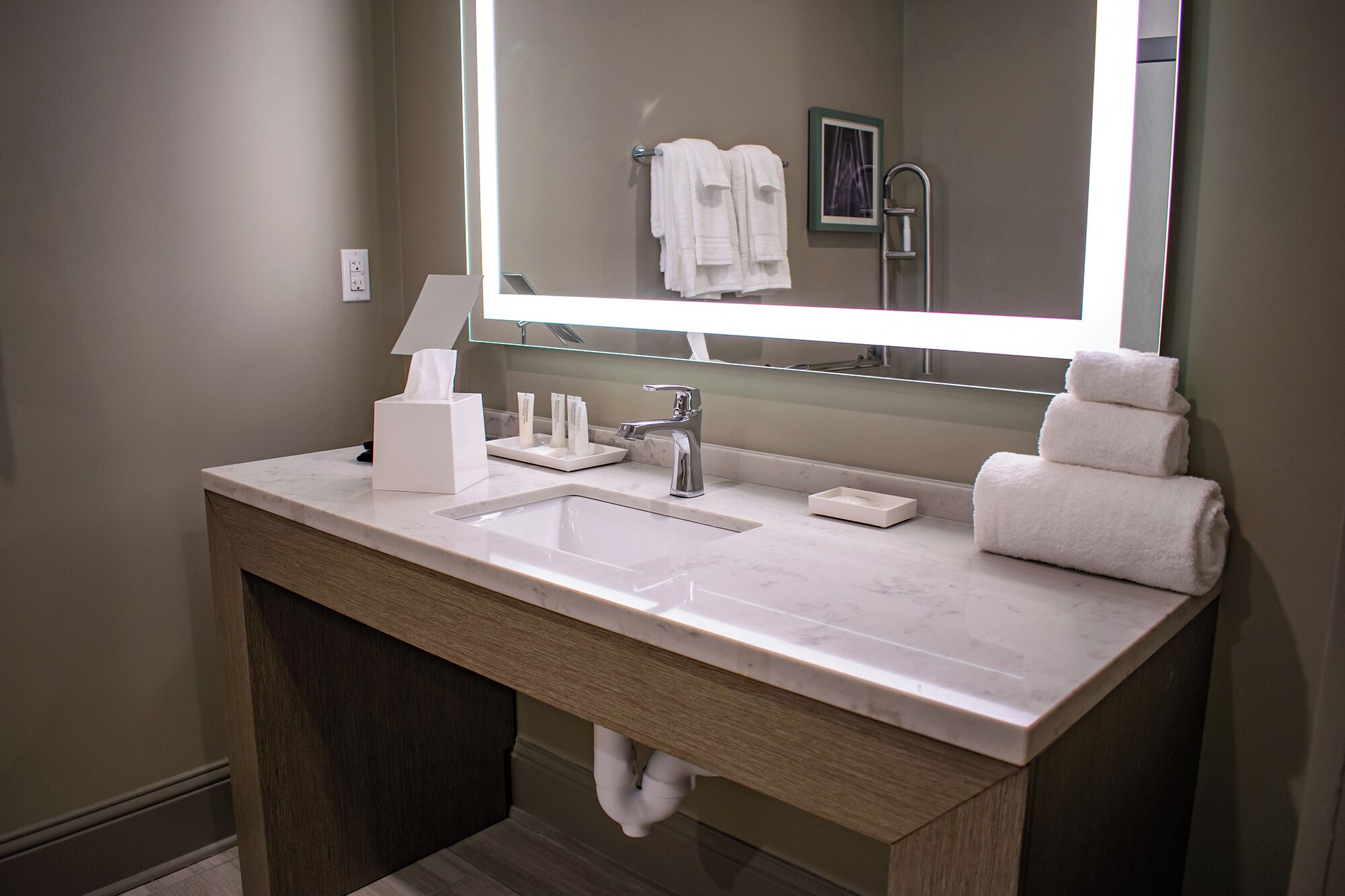 Une salle de bain moderne avec un grand miroir, un lavabo, un porte-serviettes et un support à papier toilette.
