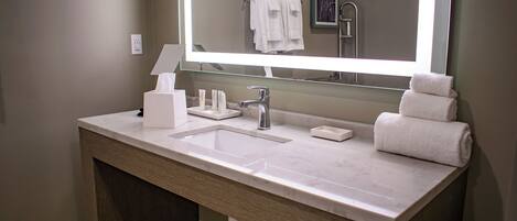Une salle de bain moderne avec un grand miroir, un lavabo, un porte-serviettes et un support à papier toilette.