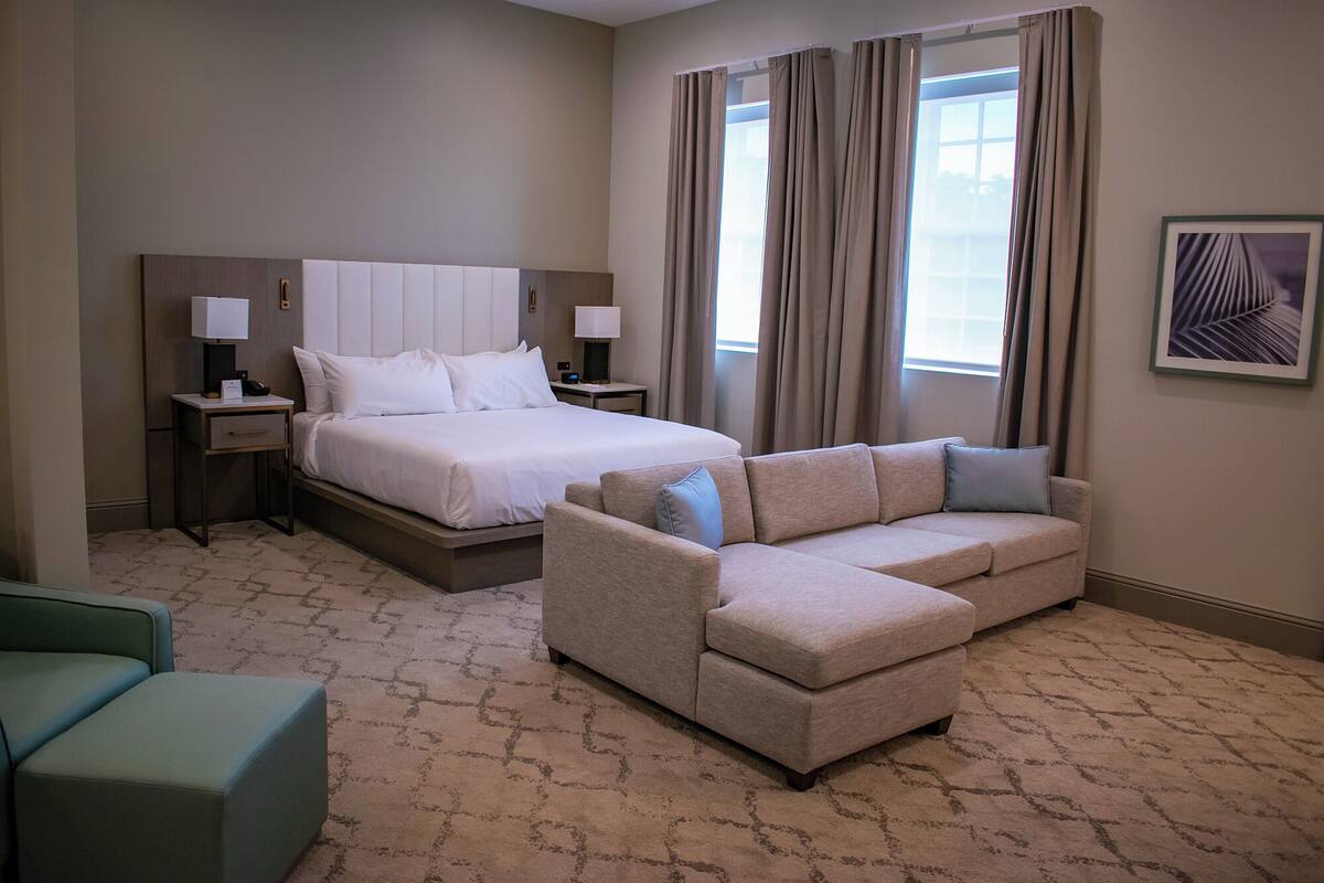 A hotel room with a bed, a sofa, a desk, and a window with curtains.